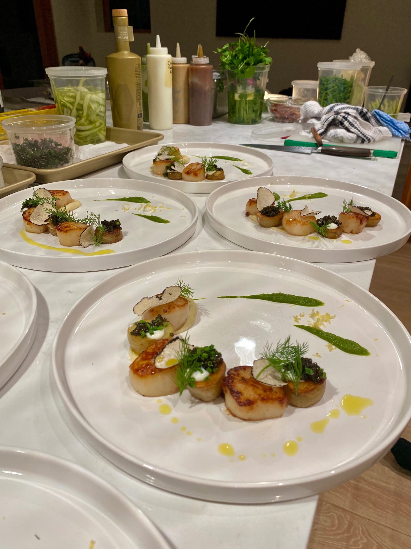 Seared scallops with caviar, black truffle and dill plated on white ceramic