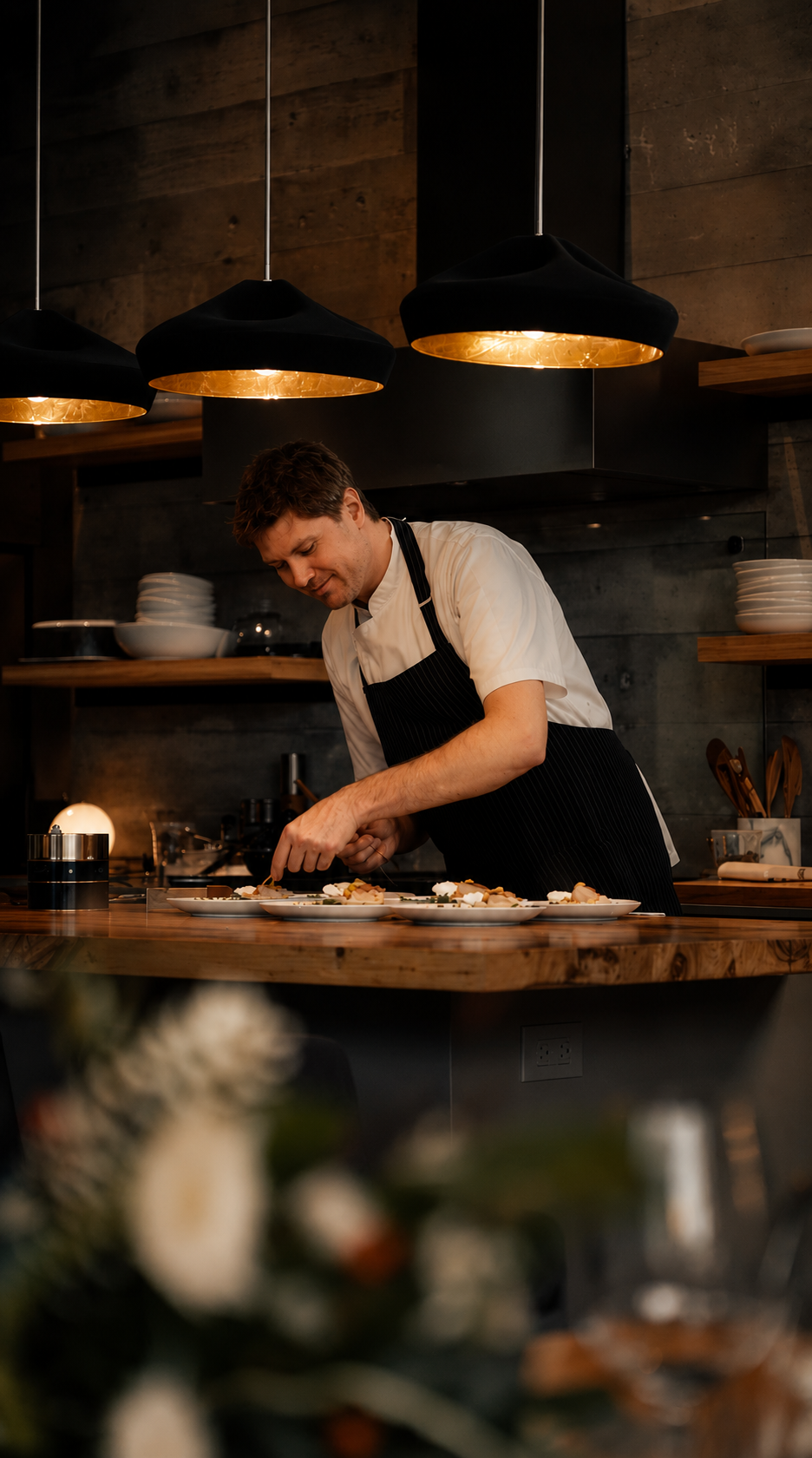 Chef Michaël plating courses in a luxury kitchen under warm pendant lights