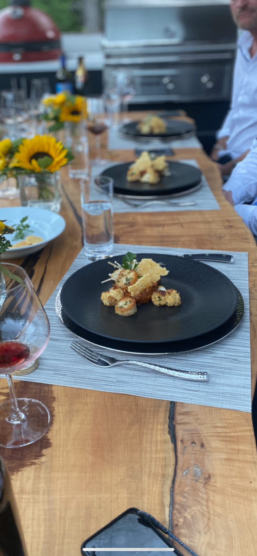 Plated seared scallops on a black plate at an outdoor chef's table